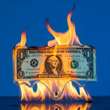 One-dollar bill burning in flames, symbolizing the financial struggles and chaos in Trump’s economy.