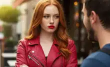 Woman in a red leather jacket with crossed arms, staring intensely, representing frustration in a relationship where someone isn’t worth your time.